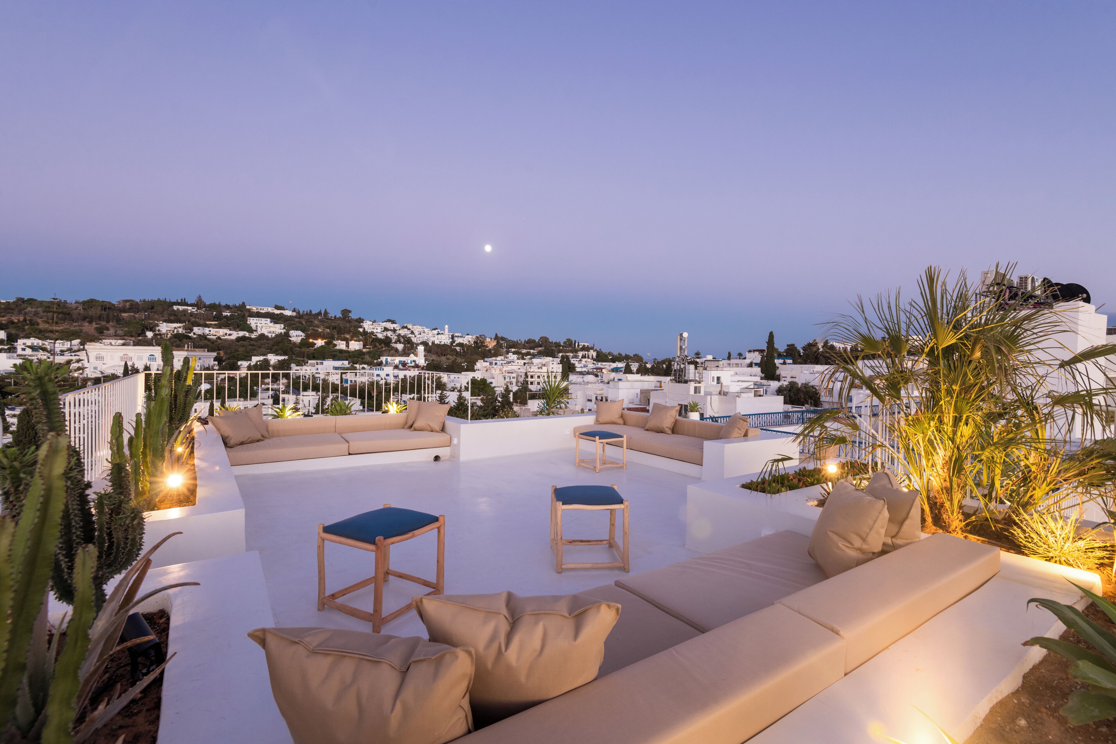 Terraza en la azotea con sofá, sillas y una mesita, con vistas a un pueblo costero con edificios y cielo despejado.