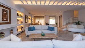A spacious living room with a white sofa set, a coffee table, and a staircase leading to an upper level.