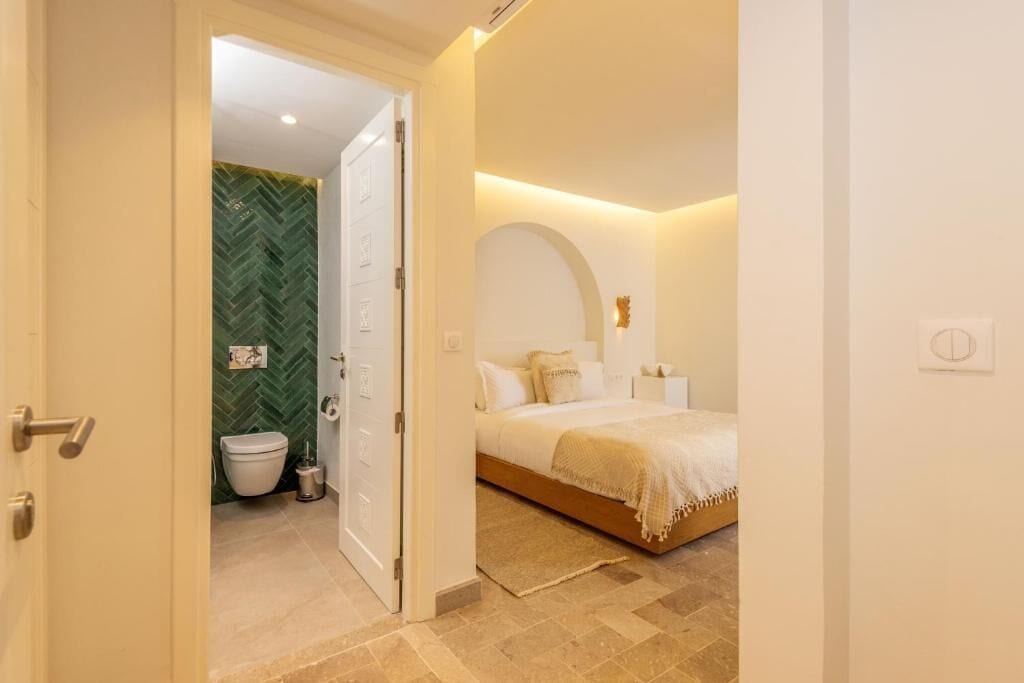 A bedroom with a bed, a bedside table, a nightstand, and a wall-mounted light fixture.