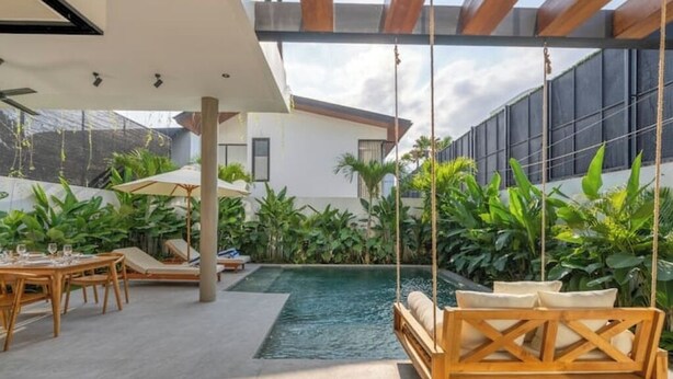 A modern outdoor pool area with a swing chair, lounge chairs, and a dining table. - Casa Riva by GORO (Bali)