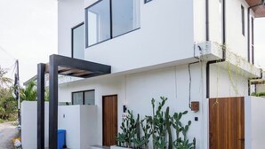 A modern two-story house with a white exterior, large windows, and a wooden door. There are cacti planted along the front wall. - Casa Riva by GORO (Bali)