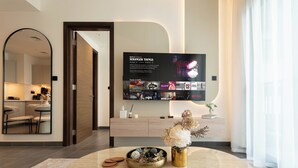A modern living room with a flat-screen TV displaying 'Stranger Things' on Netflix, a round coffee table with decorative items, and a minimalist kitchen in the background. - Chic 1BR Apartment - The Crest Dubai (Dubai)