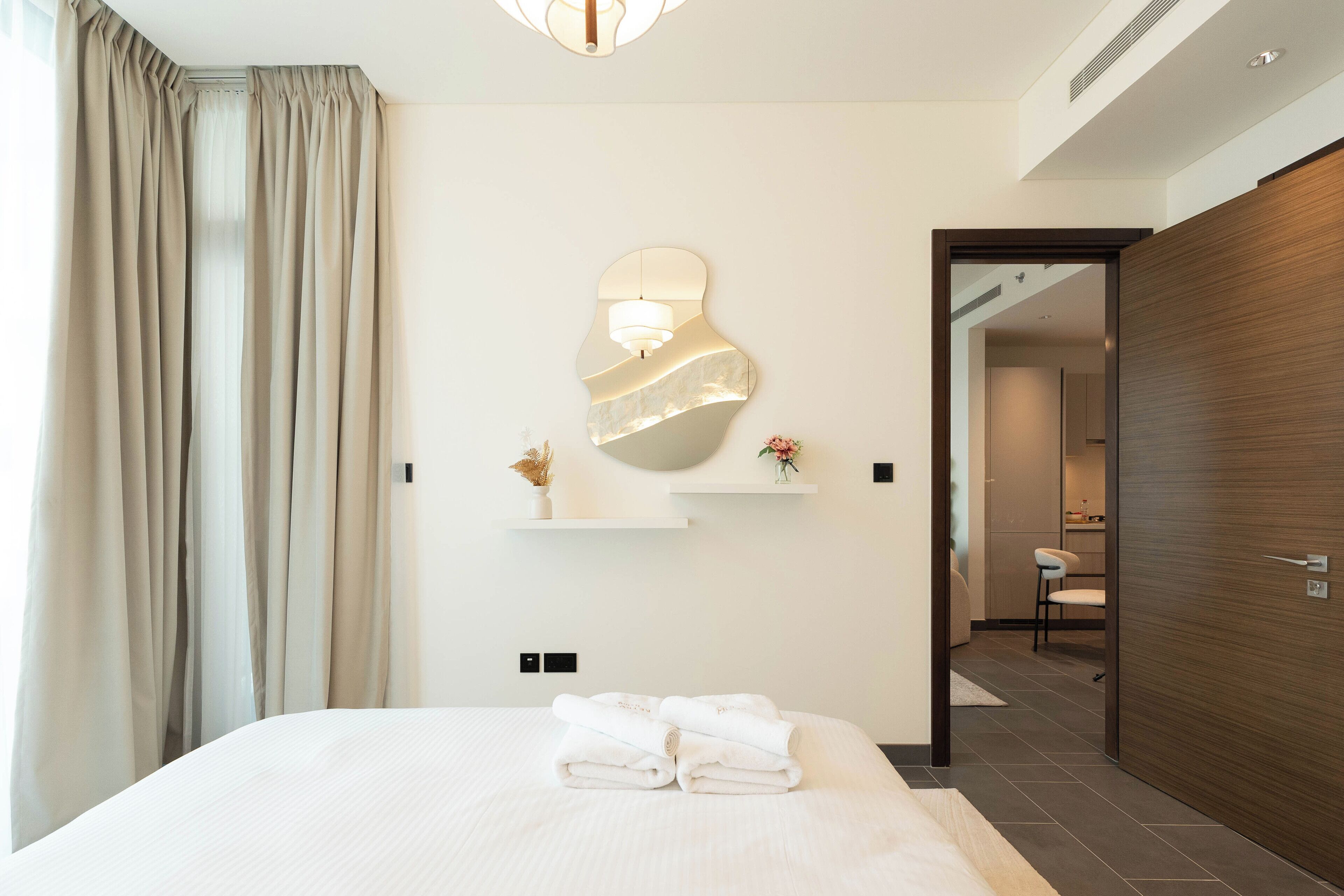 A modern hotel room with a neatly made bed, a large mirror, and a wooden door.