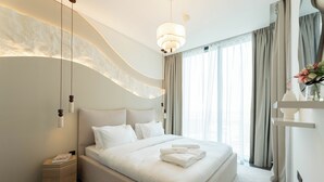 Ein modernes Schlafzimmer mit einem großen Bett, einem Nachttisch, einer Stehlampe und einem Fenster mit Vorhängen.