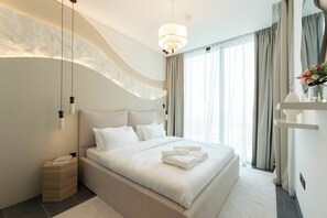 Une chambre moderne avec un grand lit, une table de chevet, une commode, un luminaire suspendu et une fenêtre avec des rideaux.