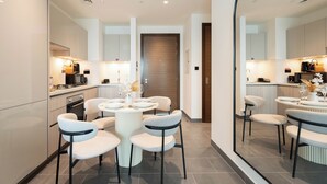 A modern kitchen with a dining area, featuring a round table with chairs, a built-in oven, and a microwave. - Chic 1BR Apartment - The Crest Dubai (Dubai)