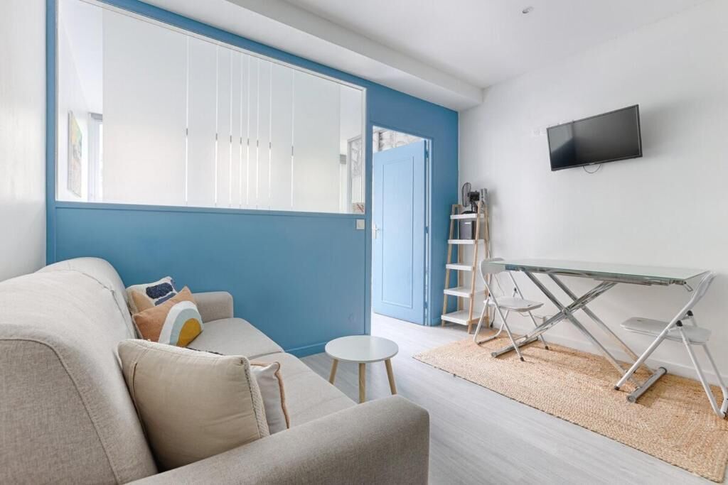 A modern living room with a sofa, a small round table, a glass-top coffee table, a TV mounted on the wall, and a blue accent wall.