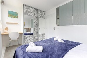 A bedroom with a bed, two towels, a desk, a chair, a mirror, and a door with a patterned curtain. - Charming apartment Gambetta - Saint Fargeau II (Paris)