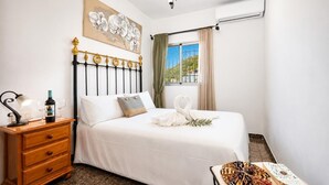A bedroom with a bed, a nightstand, a window with curtains, a chandelier, and a view of the outside. - Villa Alvarez - Three Bedroom Villa, Sleeps 6 (Almuñécar)