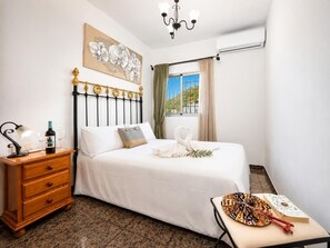 A bedroom with a bed, a nightstand, a window with curtains, a chandelier, and a view of the outside. - Villa Alvarez - Three Bedroom Villa, Sleeps 6 (Almuñécar)