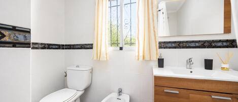 A bathroom with a toilet, bidet, vanity with a mirror, and a window with curtains.