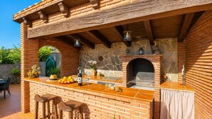 A brick outdoor kitchen with a stone wall, a built-in grill, and a bar area with stools. - Villa Alvarez - Three Bedroom Villa, Sleeps 6 (Almuñécar)