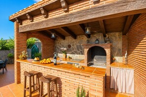 A brick outdoor kitchen with a stone wall, a built-in grill, and a bar area with stools. - Villa Alvarez - Three Bedroom Villa, Sleeps 6 (Almuñécar)