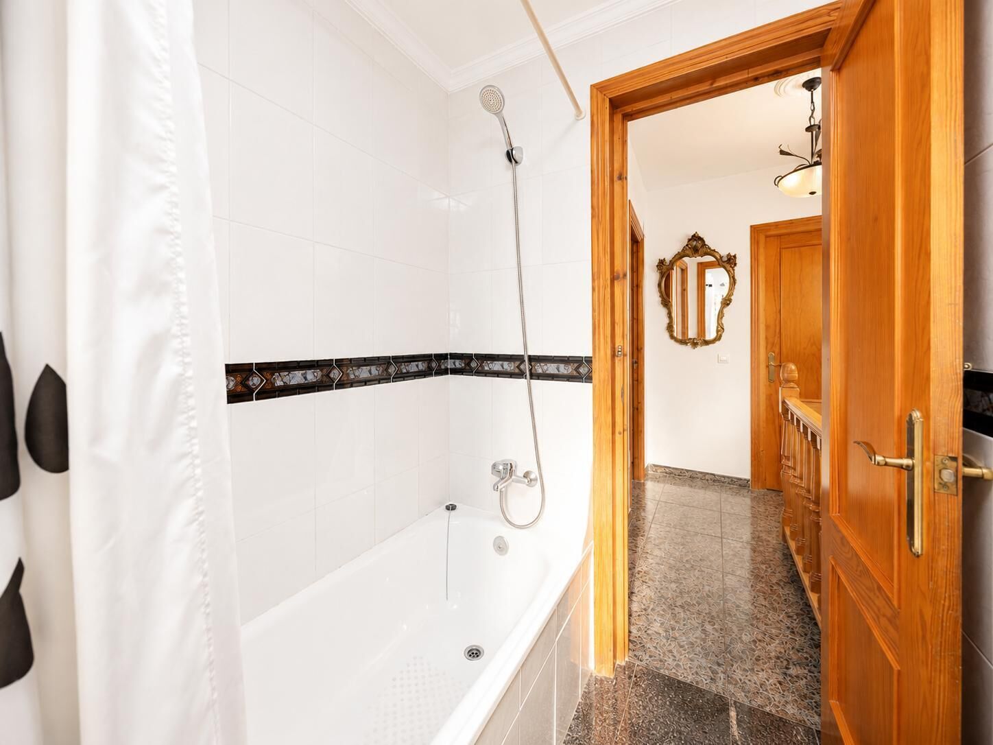 A bathroom with a bathtub, shower, and a wooden door leading to another room.