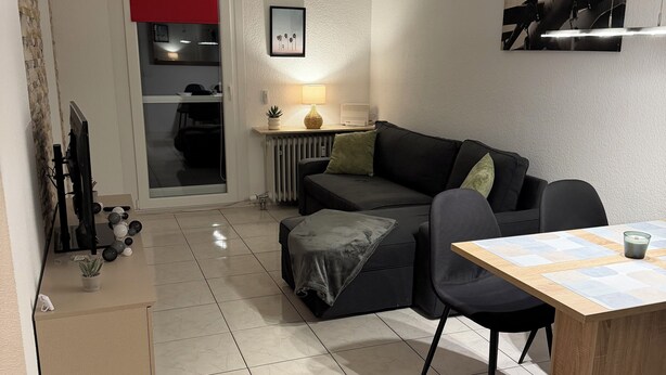 A modern living room with a black sofa, a wooden dining table, and a red curtain.