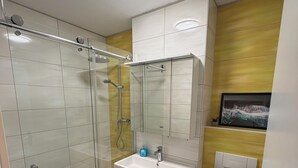 A modern bathroom with a glass shower enclosure, a white sink with a mirror above, and a toilet.