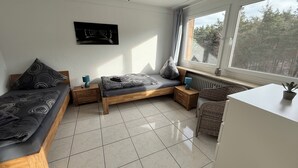A bedroom with a bed, a desk, a chair, a radiator, and a window with a view of trees.