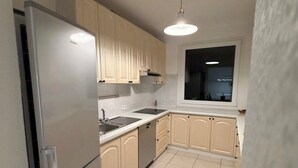 A kitchen with beige cabinets, a stainless steel refrigerator, a sink, and a window.