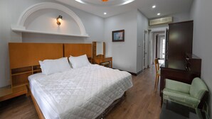 A bedroom with a large bed, wooden headboard, a desk, a chair, and a television.