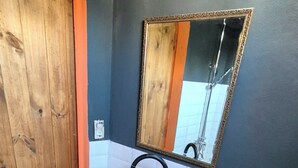 Een badkamer met een houten deur, een zwart wastafelmeubel met een spiegel erboven en een wit toilet.