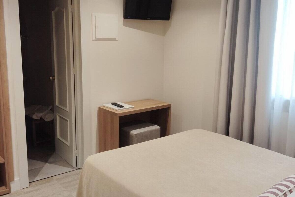 A hotel room with a bed, a desk, a television mounted on the wall, and a door leading to a closet.