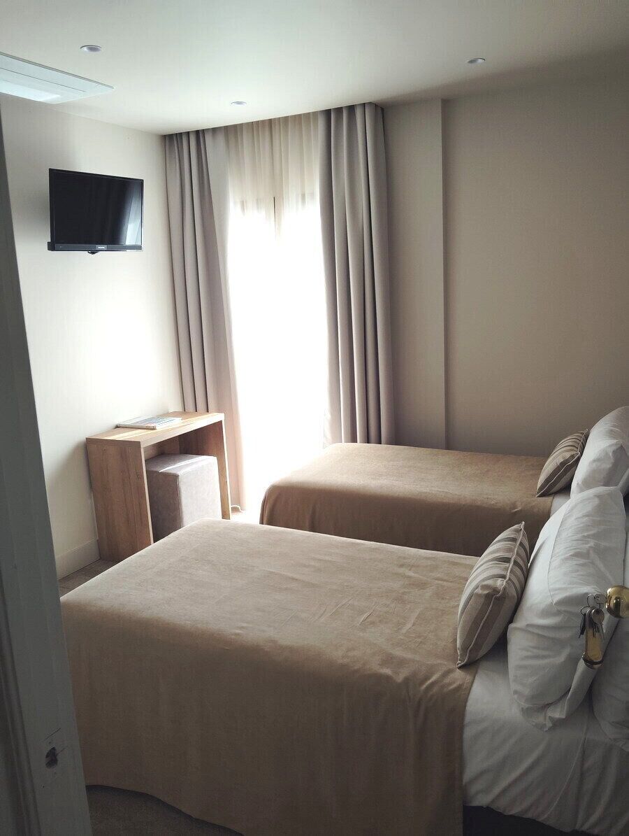 Een hotelkamer met twee bedden, een bureau, een televisie en een raam met gordijnen.