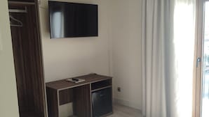 Ett rum med en platt-TV som är monterad på väggen, ett skrivbord i trä med en stol, en garderob och en skjutdörr i glas till höger.