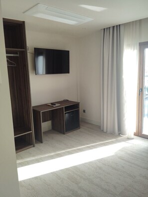 A room with a flat-screen TV mounted on the wall, a wooden desk with a chair, a wardrobe, and a sliding glass door to the right. - Hotel Velez (Velez Rubio)