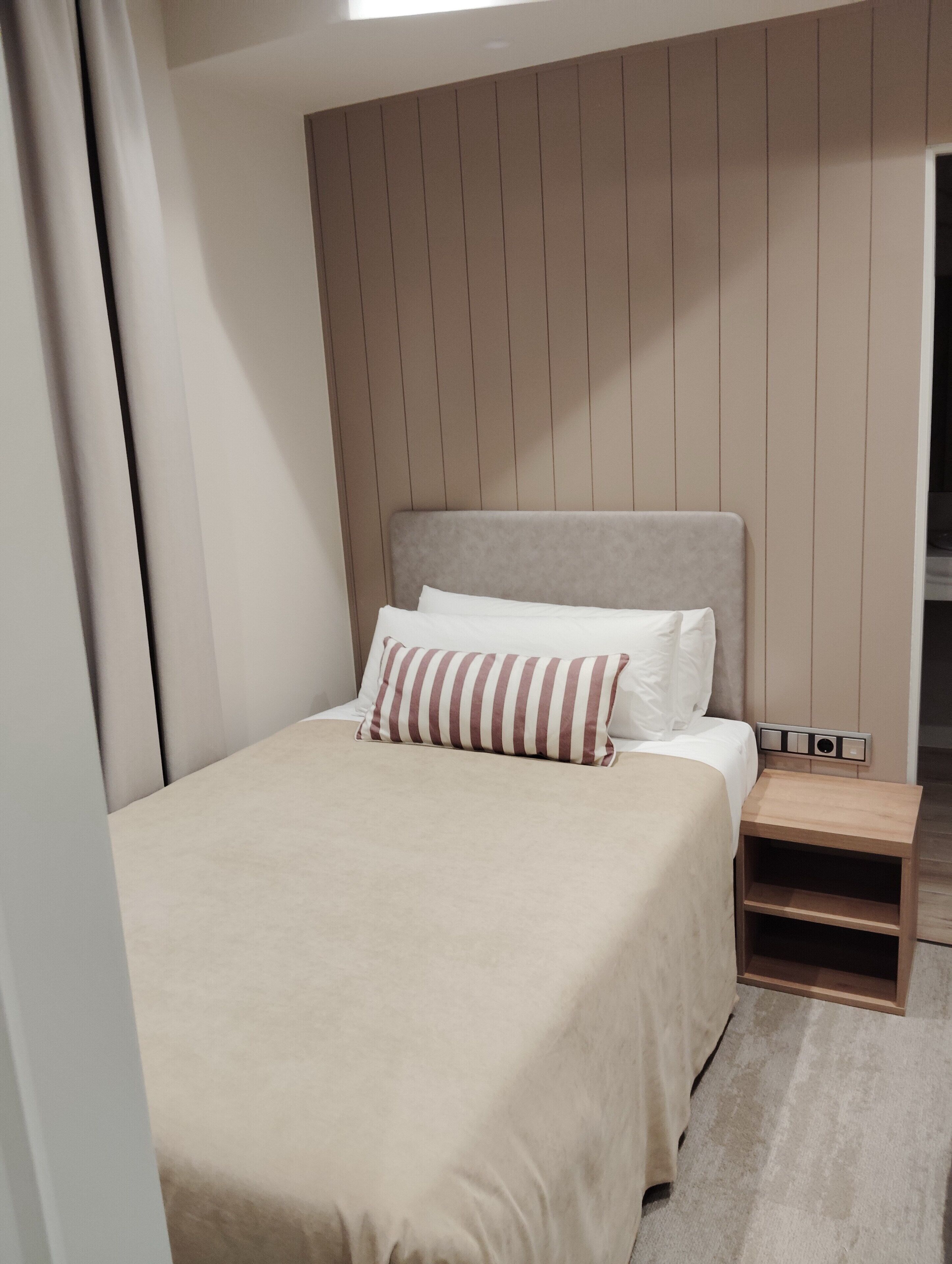 A bedroom with a bed, a bedside table, and a wall-mounted control panel.