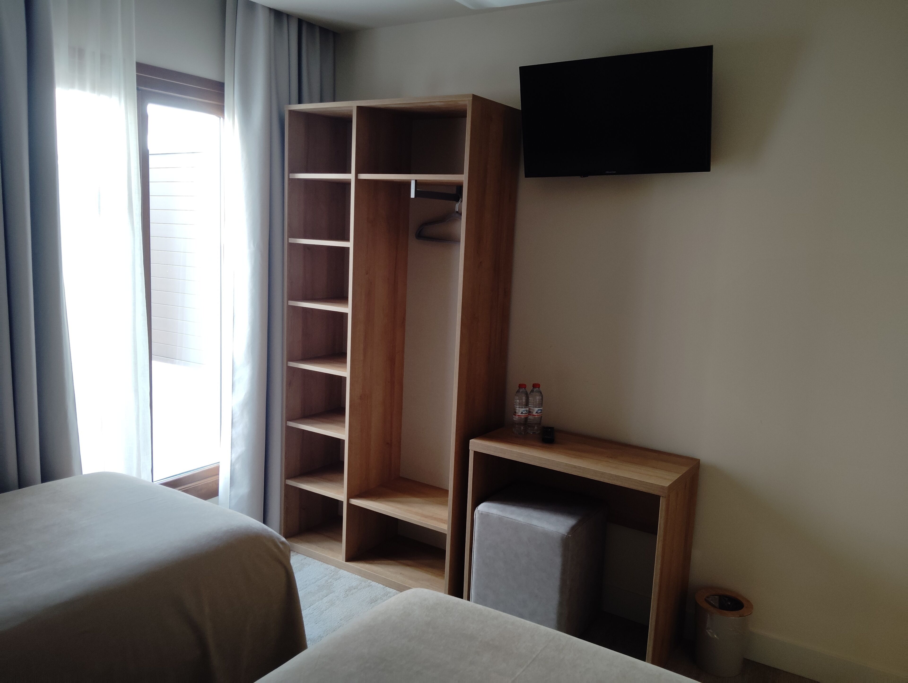 Une chambre d’hôtel avec une grande armoire en bois, un téléviseur à écran plat, une petite table avec deux bouteilles et deux lits.