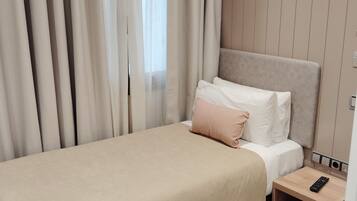 A neatly made bed with a beige bedspread, a single white pillow, and a pink pillow. There is a wooden nightstand with a remote control on it.