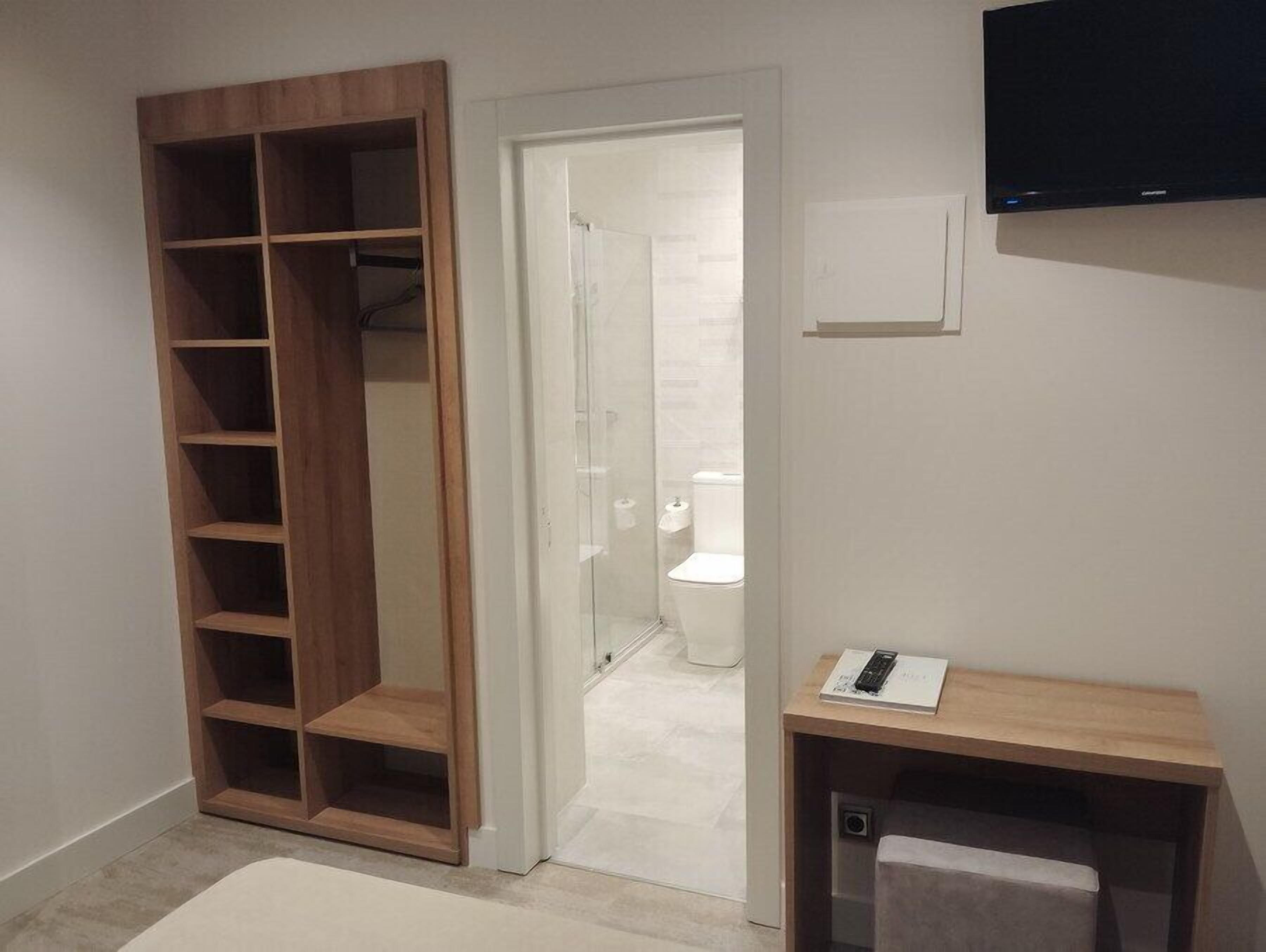 Un baño con inodoro, ducha y estantería de madera.