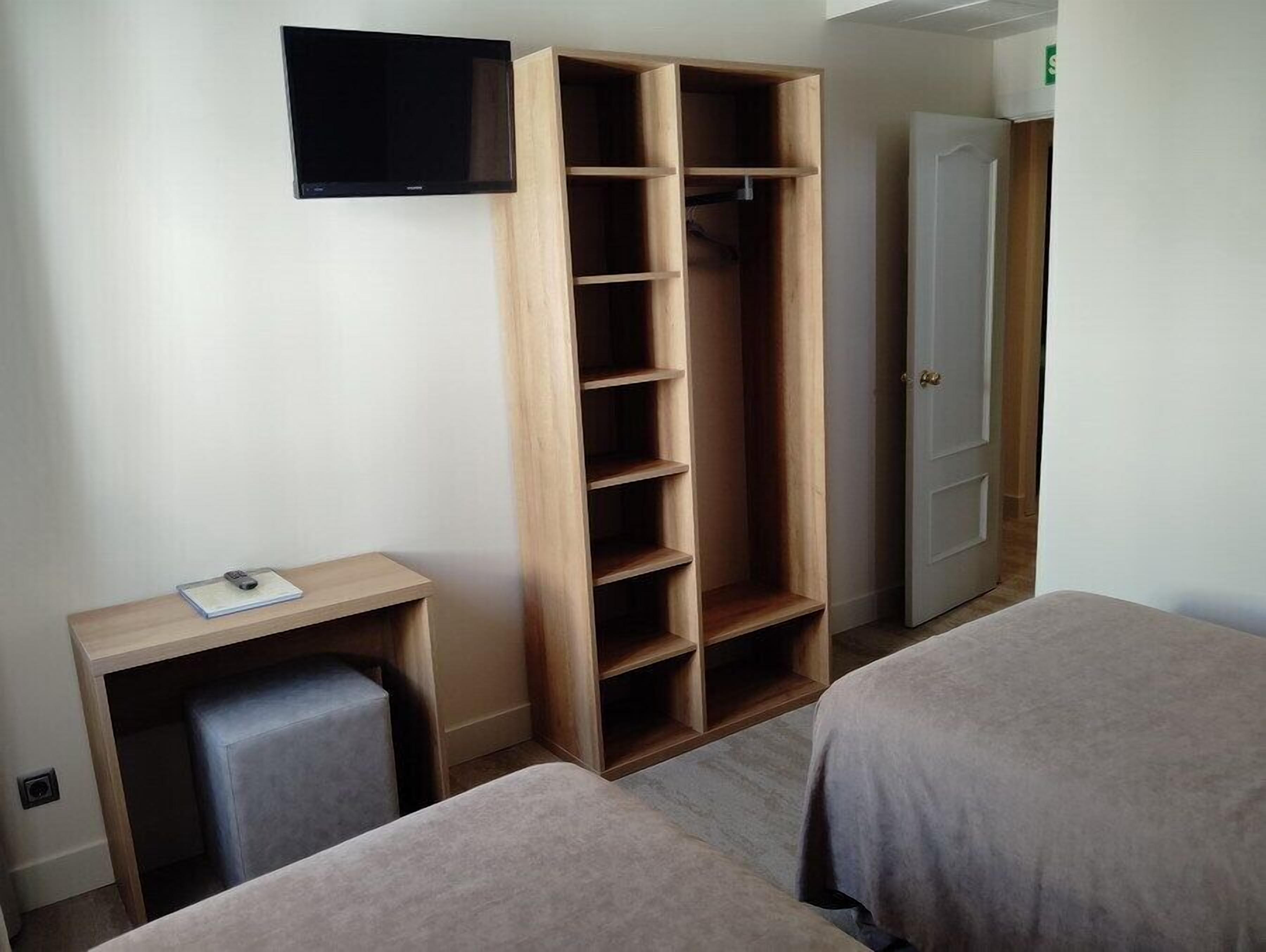 A hotel room with a TV, a wooden wardrobe, a desk with a chair, and two beds.