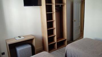 A hotel room with a TV, a wooden wardrobe, a desk with a chair, and two beds.