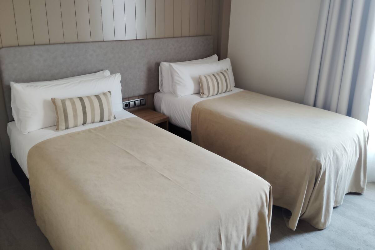 A hotel room with two beds, a nightstand, and a headboard with vertical lines.