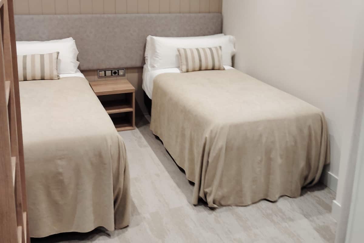 A bedroom with two single beds, a nightstand, and a wooden headboard.