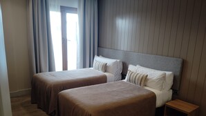 Ett hotellrum med två sängar, ett träbord vid sängen och en dörr med gardiner.