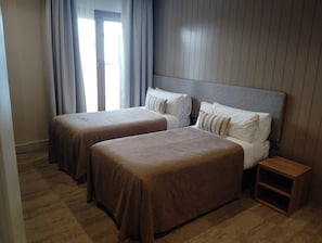 Una habitació d'hotel amb dos llits, una taula de nit de fusta i una porta amb cortines.