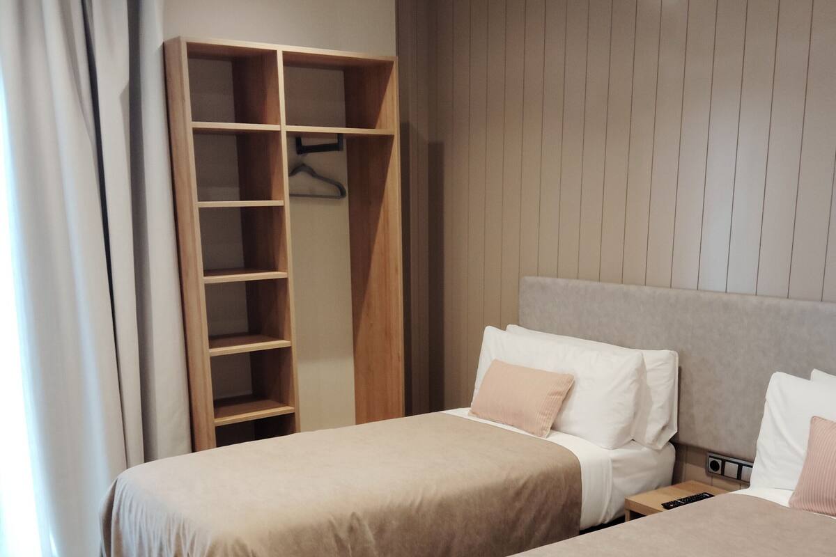A hotel room with two beds, a wardrobe, a bedside table, and a headboard.