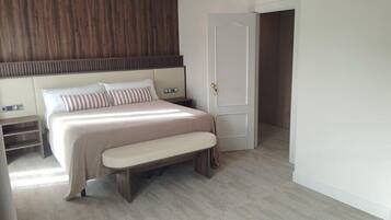 Un dormitorio con cama, banco, mesita de noche y una puerta que indica 'SALIDA'.