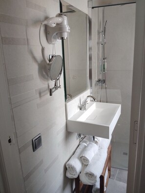 A bathroom with a white sink, a mirror, a hairdryer, and a shower.