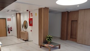 En modern entréhall med ett marmorgolv, träpanel, en receptionsdisk, en spegel och en krukväxt.