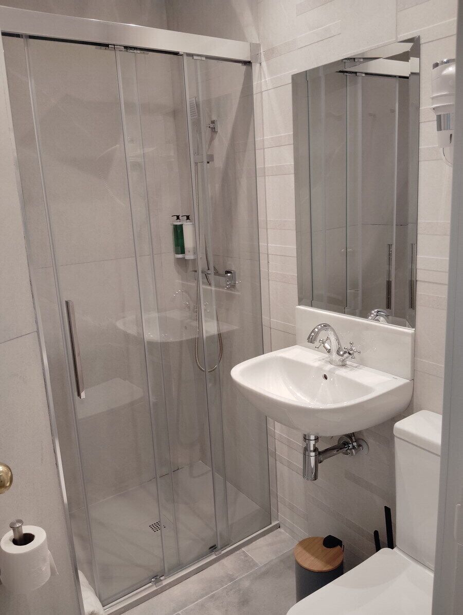 Ein modernes Badezimmer mit Duschkabine aus Glas, einem weißen Waschbecken und einem großen Spiegel.