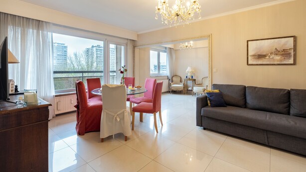 A modern living room with a grey sofa, a dining table with red chairs, and a chandelier. - Brussels Expo Elegant residence (Brussels)