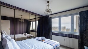 A bedroom with a large bed, a mirror, a chandelier, and a view of buildings through a window. - Brussels Expo Elegant residence (Brussels)