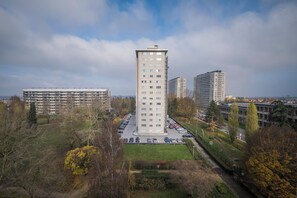 Un immeuble de grande hauteur avec un parking à l’avant, entouré d’arbres et d’autres bâtiments.