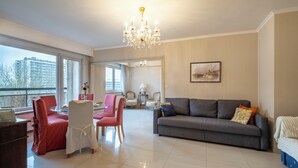 A spacious living room with a grey sofa, red chairs, a chandelier, and a large window offering a city view. - Brussels Expo Elegant residence (Brussels)