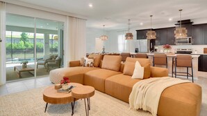 A modern living room with a large sectional sofa, a coffee table, and a dining area with bar stools. - 7‑BR w/ Private Pool & Game Room (Kissimmee)