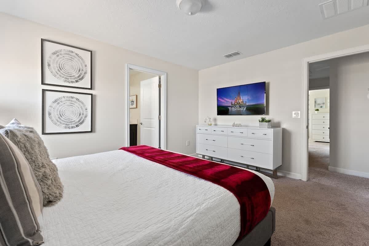 A bedroom with a large bed, a TV on the wall, and a dresser.