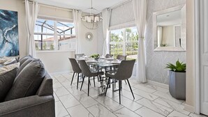 A dining area with a glass table and chairs, a chandelier, and a view of the outdoors. - 5BR Home w/ Private Pool - Storey Lake Resort (Kissimmee)